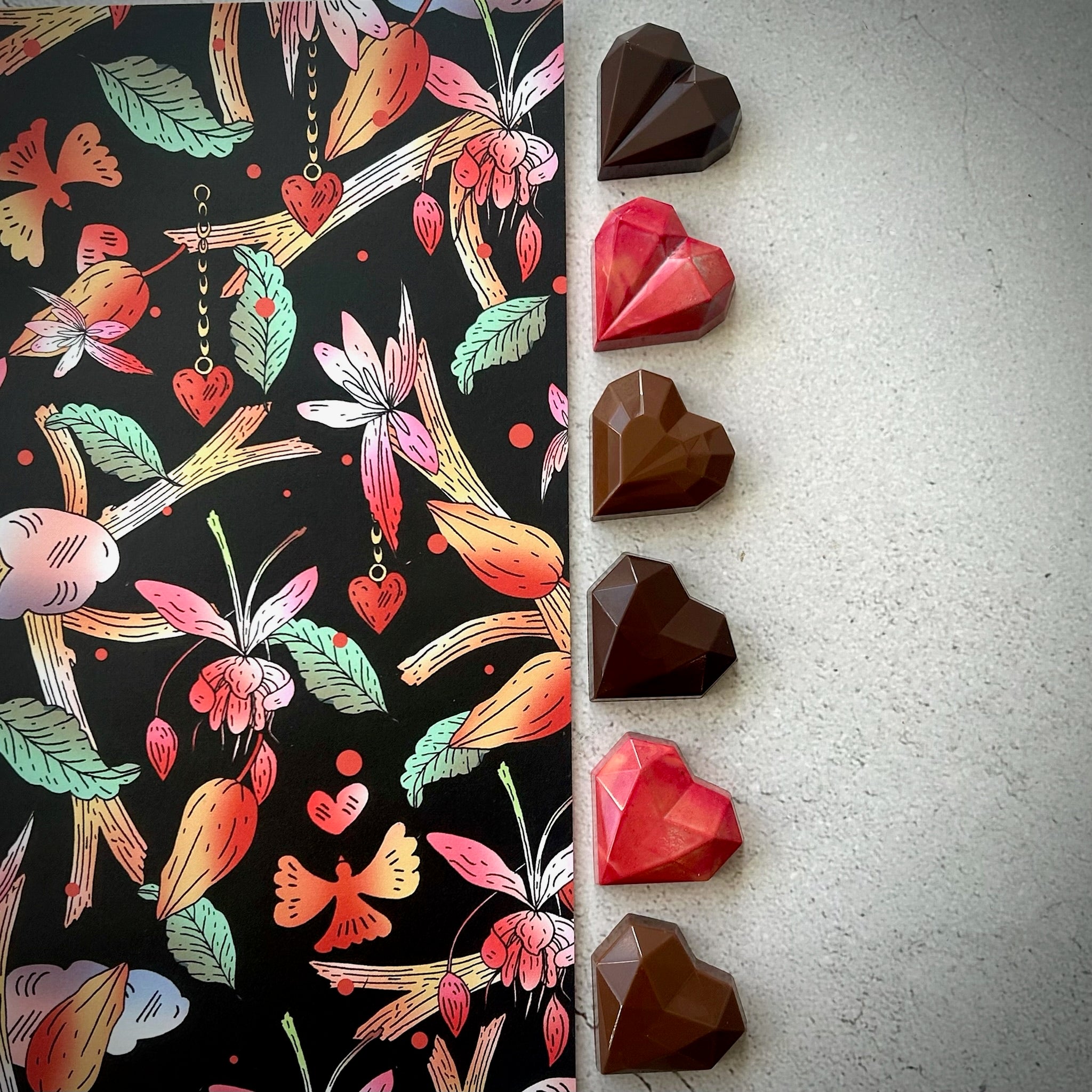 Chocolats artisanaux en forme de cœur, rouges et bruns, alignés à côté d’un emballage illustré. Le coffret contient 2 cœurs caramel, 2 cœurs praliné maison, et 2 cœurs gelée d’airelle et praliné amandes. Créés à Montréal pour la Saint-Valentin.