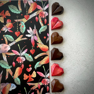 Chocolats artisanaux en forme de cœur, rouges et bruns, alignés à côté d’un emballage illustré. Le coffret contient 2 cœurs caramel, 2 cœurs praliné maison, et 2 cœurs gelée d’airelle et praliné amandes. Créés à Montréal pour la Saint-Valentin.